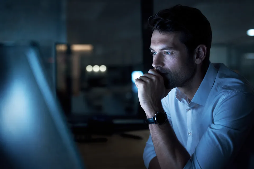 Equity analyst lit by a monitor in a dark office at night